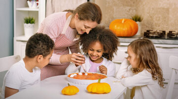 Mom and three children at kitchen table decorating pumpkin dessert for a blog about trader joe's fall recipes