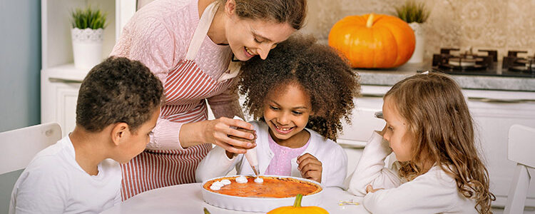 Mom and three children at kitchen table decorating pumpkin dessert for a blog about trader joe's fall recipes